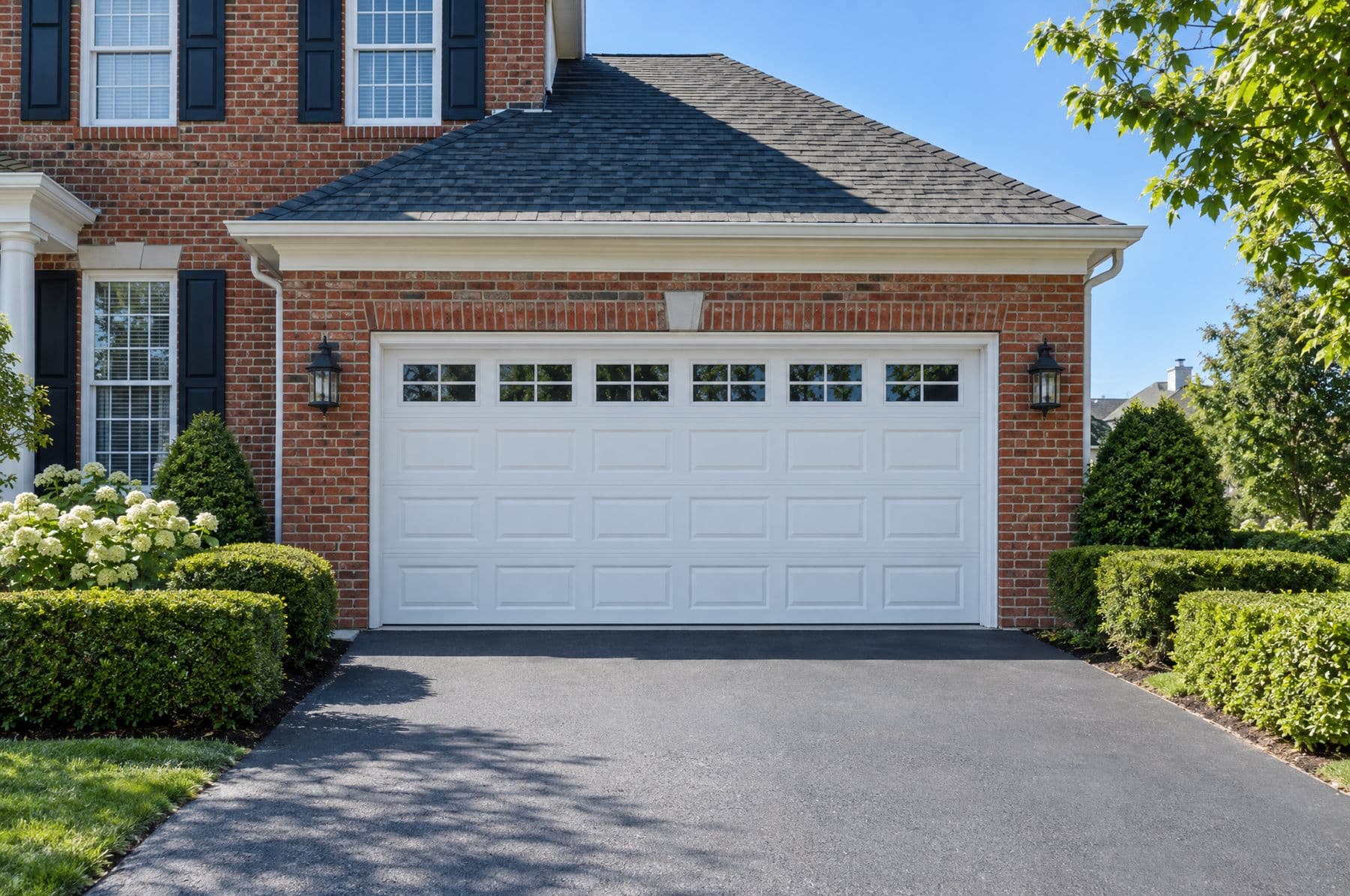 A white raised-panel garage door on a brick colonial home